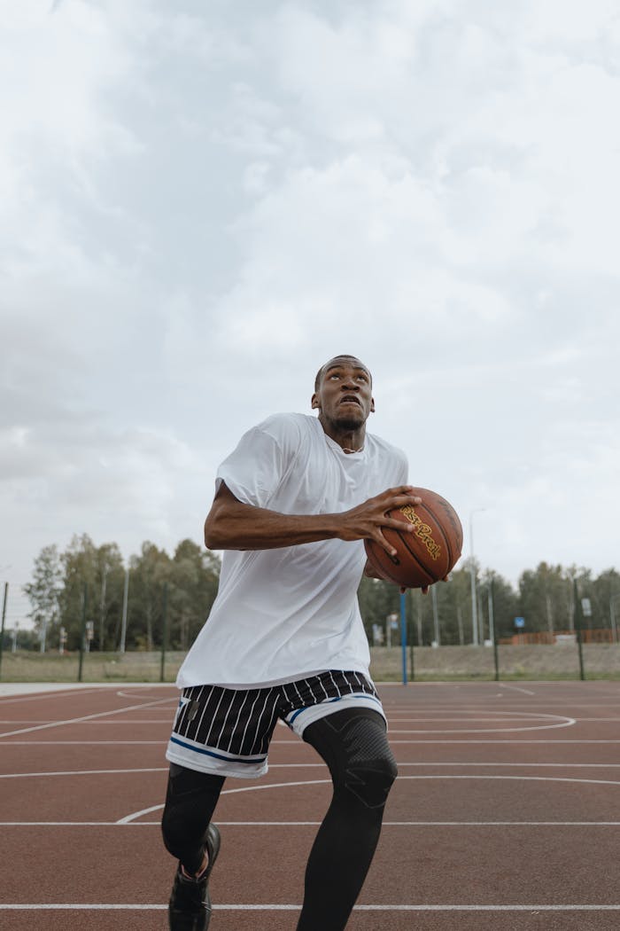 A focused athlete in activewear prepares for a layup on an outdoor basketball court under cloudy skies.