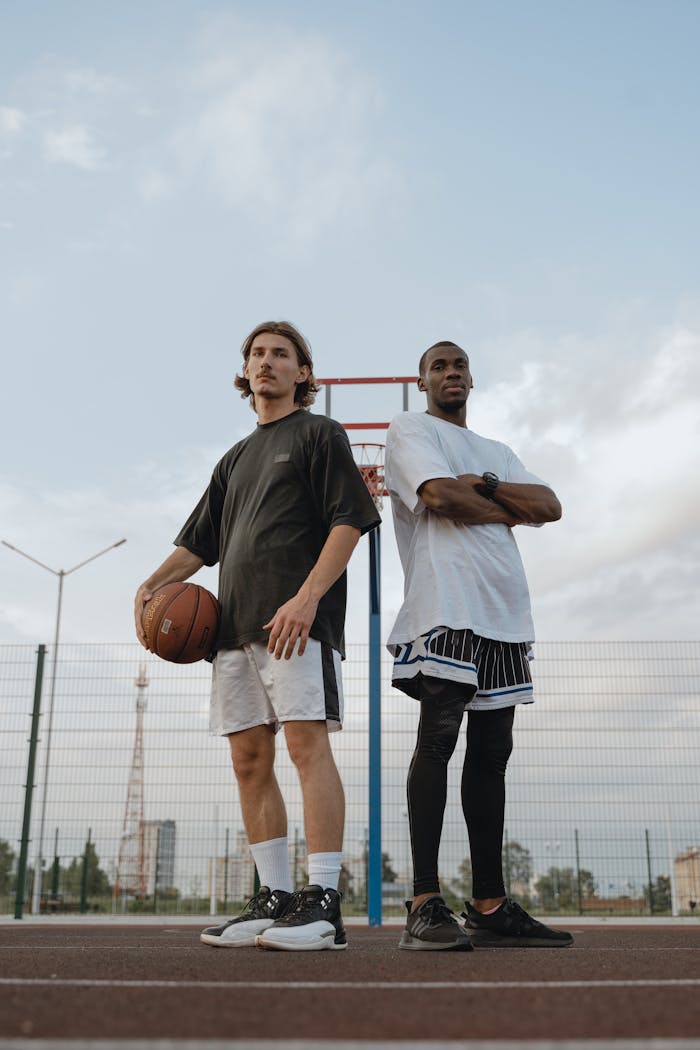Two basketball players confidently pose on an outdoor court, showcasing their athletic skills.